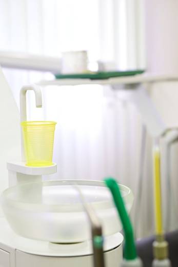 Nahaufnahme einer zahnärztlichen Behandlungseinheit mit gelbem Kunststoffbecher unter einem Wasserspender.