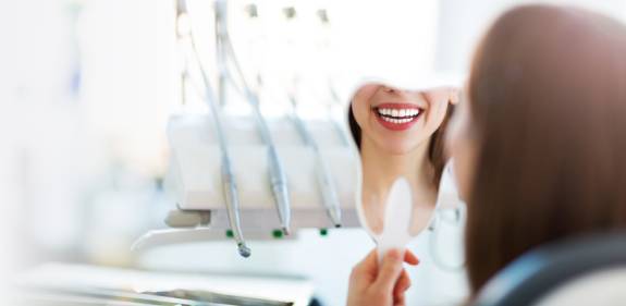 Eine Patientin beim Zahnarzt betrachtet ihr Lächeln in einem Handspiegel