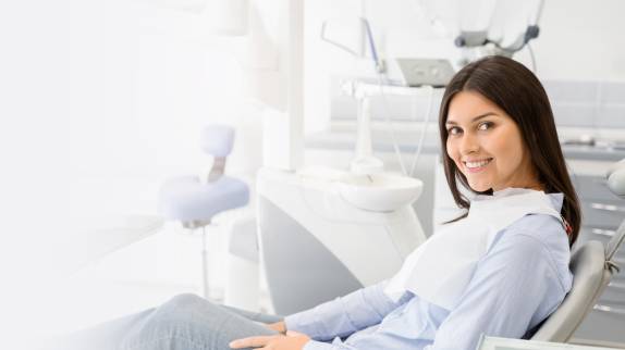 Junge Frau sitzt entspannt auf einem Behandlungsstuhl in einer Zahnarztpraxis und lächelt freundlich in die Kamera