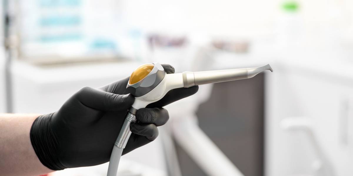 Hand in schwarzem Handschuh hält ein professionelles zahnmedizinisches Reinigungsgerät in moderner Zahnarztpraxis