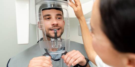 Ein junger Mann wird von einer Zahnärztin für eine digitale Röntgenaufnahme mit einem modernen 3D-Panorama-Röntgengerät positioniert